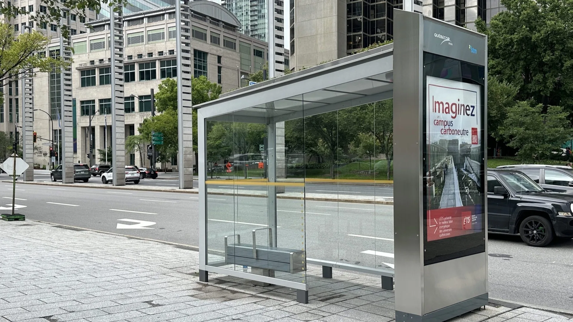 Modern glass bus shelter with stainless steel frame and STM digital advertising panel on a downtown Montreal street